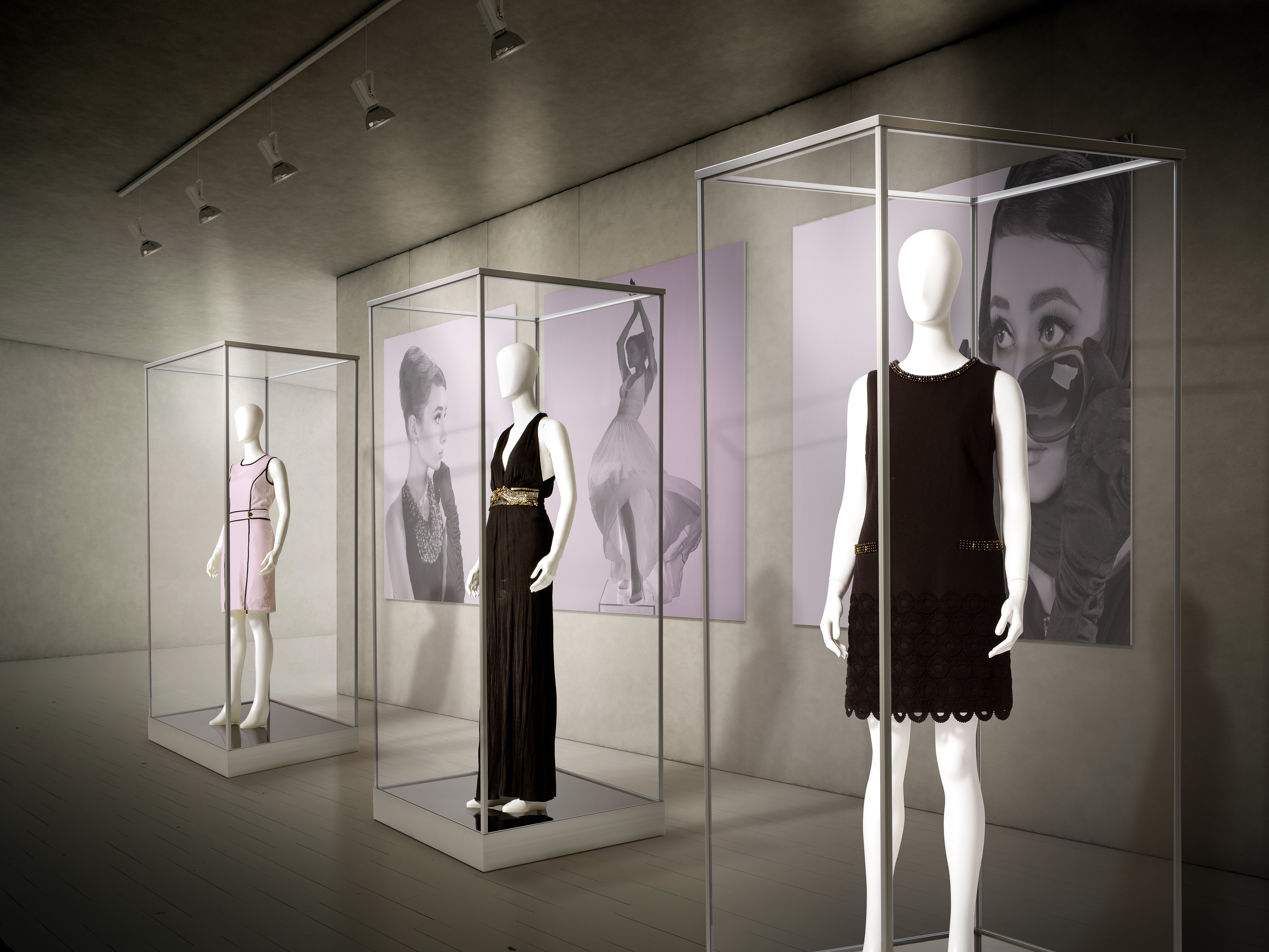 A trio of single tower acrylic echibit cases each containing a mannequin wearing a dress